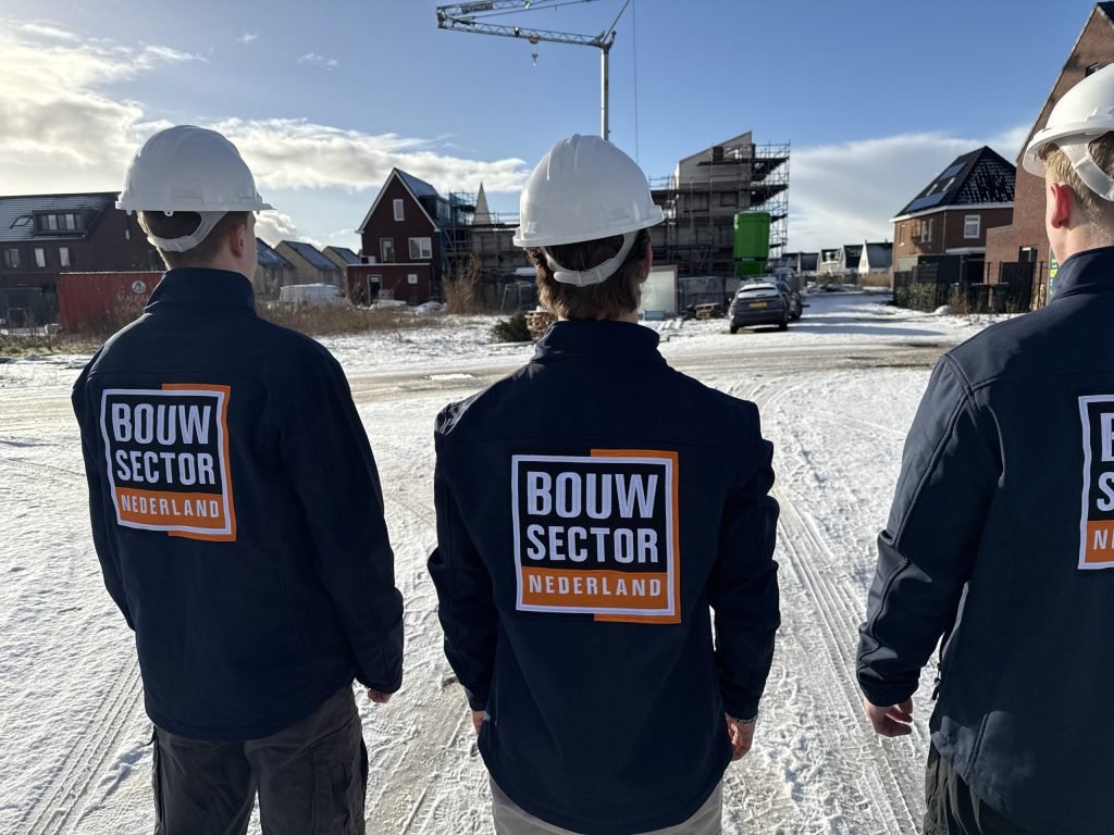 Drie vakmensen van Bouwsector Nederland met witte helm kijken naar nieuwe huizen in aanbouw